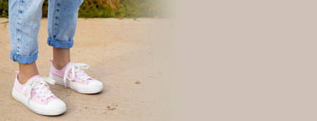 A view of the legs of a teenage girl in pink sneakers and blue jeans against a background of yellow...