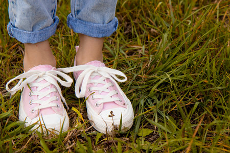 A view of the legs of a teenage girl in pink sneakers and blue jeans against a background of yellow dry grass. The concept of clothing for modern teenagers, even in the cool seasonの写真素材