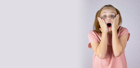 Portrait Surprised little girl holding her cheeks with her hands. Place for text. Banner.の写真素材