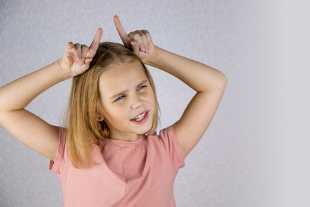 A little charming fair-haired girl shows small horns with her hands and expresses different emotions. Place for textの写真素材