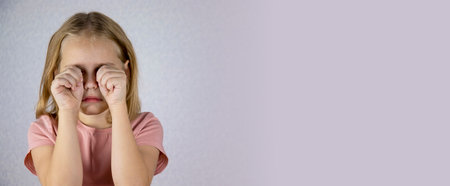 Portrait of a girl, she rubs her small eyes with her hands. Bad mood, tears and negative emotions. Banner.の写真素材