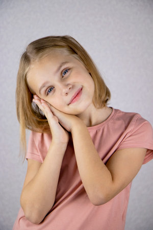 Portrait of a cute girl on a light background, a little blonde looks at the camera and smiles. The concept of joy, happiness and good moodの写真素材