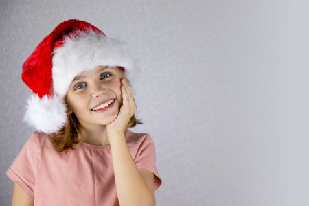 Portrait of a cute little girl with a wide smile in a santa hat on a light background. Merry Christmas, holidays.の写真素材