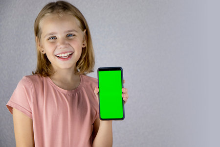 Portrait of a little blonde haired girl showing a mobile phone application in her hands with a green screen. He looks into the camera and smiles widelyの写真素材
