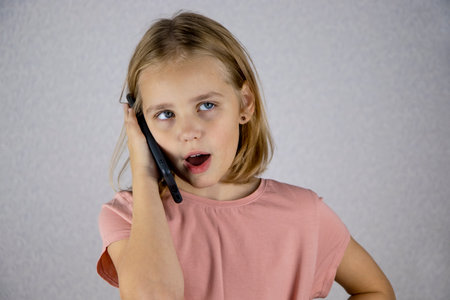 A cute little girl calls on a mobile phone and has an important and lively conversation. Emotions of the child when communicating on a smartphoneの写真素材