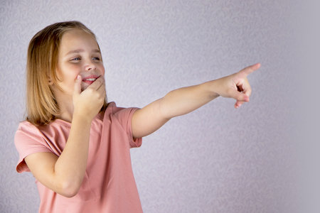 cute blonde little girl smiles covering her smile with her hand and pointing her finger. Surprise, laughter and emotions.の写真素材