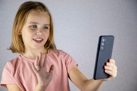 A cute little girl is calling on a smartphone and talking on a video link. Online communication, friendship and vivid emotions of children.の写真素材