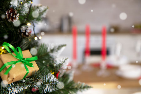 Selective focus on a Christmas bright and fluffy tree with a gift wrapped in ecological reusable paper on the background of the festive table.の写真素材