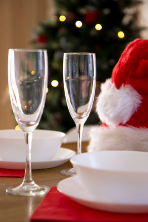 Beautiful table setting for the Christmas dinner with transparent glasses and porcelain plates against the background of the Christmas tree and Santa's hatの写真素材