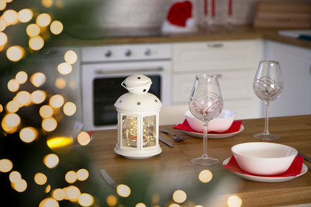 Selective focus on Beautiful table setting for Christmas dinner with transparent glasses and porcelain plates against the background of a Christmas tree and bokeh lights. Blurred background.の写真素材