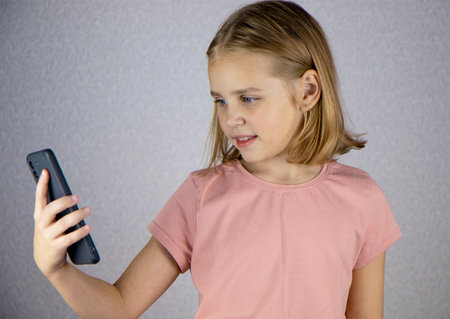 A cute little girl is calling on a smartphone and talking on a video link. Online communication, friendship and vivid emotions of children.の写真素材