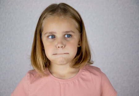 Portrait of a little thoughtful girl. She puffs out her cheeks and thinks about something, looks away.の写真素材
