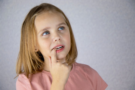 Thoughtful little girl looks away and touches her mouth with her finger. Emotions and reflectionsの写真素材