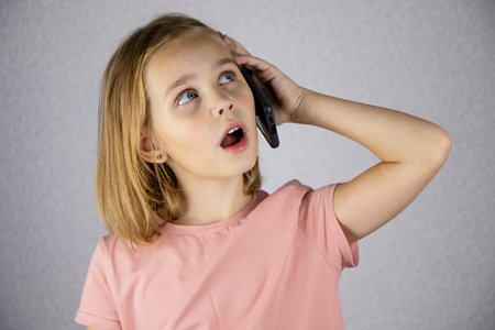 A cute little girl calls on a mobile phone and has an important conversation. Vivid emotions of a child when communicating on a smartphoneの写真素材