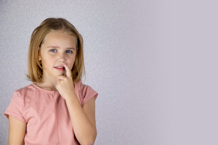 Little cute girl with blond hair picks her nose. The child clears his nose and thinks about something.の写真素材