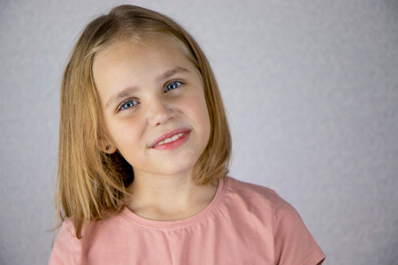 Portrait of a cute little girl on a light background, looking at the camera and smiling. The concept of joy, happiness and good moodの写真素材