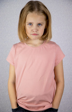 Portrait of a little offended girl looking at the camera with her hands in her jeans pockets