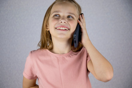 A cute little girl calls on a mobile phone rejoices and laughs. Vivid emotions of a child when communicating on a smartphoneの写真素材