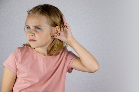 Portrait of a little blonde girl with her palm to her ear, she wants to hear or eavesdrop on...
