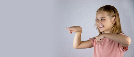 Portrait of a laughing little girl with blond hair, she shows something with her fingers. Hand signs and gestures. Place for text. Banner.の写真素材