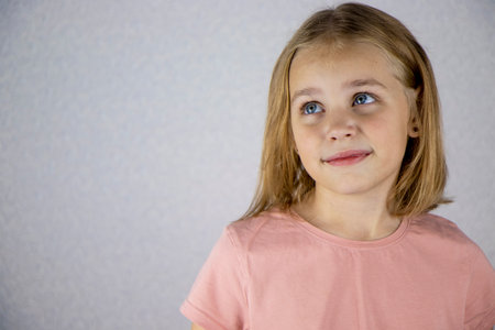 Portrait of a cute girl on a light background, a little blonde looks at the camera and smiles. The concept of joy, happiness and good moodの写真素材