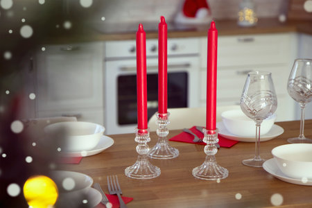 Selective focus on a beautiful table setting for Christmas dinner with transparent glasses and porcelain plates against the background of red candles and a Christmas treeの写真素材