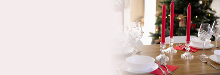 Banner. beautiful table setting for Christmas dinner and meeting with friends with transparent glasses and porcelain plates on the background of red candles and a Christmas treeの写真素材