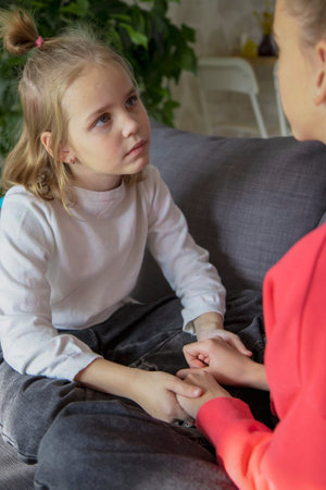 Two schoolgirl girls are sitting on the sofa in the living room and discuss misunderstandings, difficulties and family problems. Help and compassion concept.の写真素材