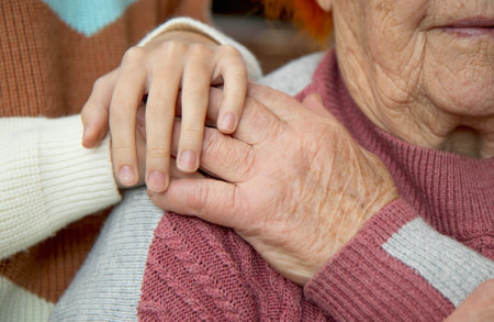The hands of an old and a young woman embrace each other. Love and care for the older generation, respect for the elderly.の写真素材