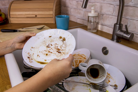 The child is in the kitchen. Small childrens hands put a dirty plate in the sink. The concept of cleaning the house, helping parents, cleanliness and orderの写真素材