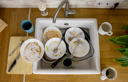 A pile of unwashed dishes in the sink. Mess and dirt in the kitchen. Dirty plates, mugs and cutlery. Putting the house in order, big cleaning, cluttered house.の写真素材