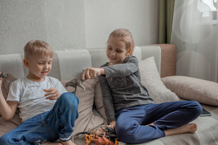 Little brother and sister are playing with plastic animals sitting on the couch and laughing merrily. Love and friendship within the family, joint leisure and development of childrenの写真素材