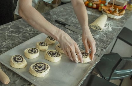 The hands of a young woman form and place delicious homemade buns desserts with poppy seeds on a...