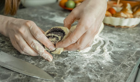 The hands of a young woman form and place delicious homemade buns desserts with poppy seeds on a baking tray. Cooking a delicious dessert at home.の写真素材