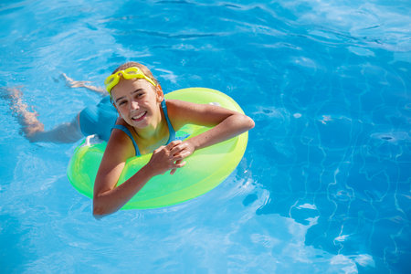 Smiling cute teenage girl wearing swimming glasses and a large swimming circle in the pool on a sunny summer day.の写真素材
