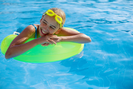Smiling cute teenage girl wearing swimming glasses and a large swimming circle in the pool on a sunny summer day.の写真素材