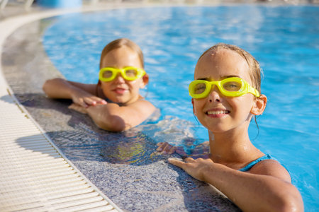 Two cute little sister girls wearing glasses for swimming in the pool on a sunny summer day. Selective focusの写真素材