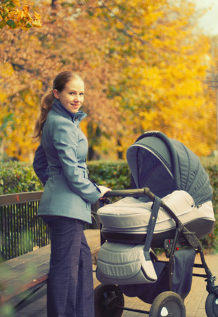 young mother with a pram on a walk in the park in autumn