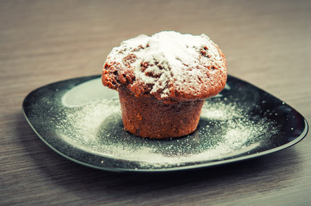 Muffin chocolate cake with white powdered sugar on a black plateの写真素材