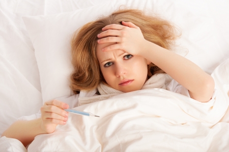Woman with thermometer sick colds, flu, fever and migraine in bedの写真素材