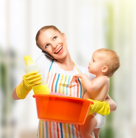 young happy mother is a housewife with a baby does homework and talking on the phone at homeの写真素材