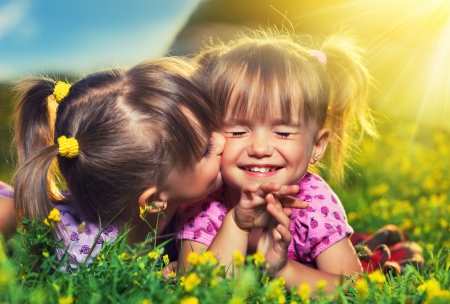 happy family. little girls twin sisters kissing and laughing in the summer outdoorsの写真素材