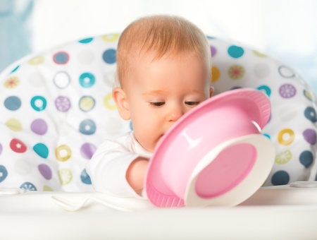 A funny baby is eating from pink plateの写真素材