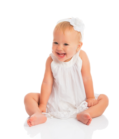 happy little baby girl in white dress laughs isolated on white backgroundの写真素材