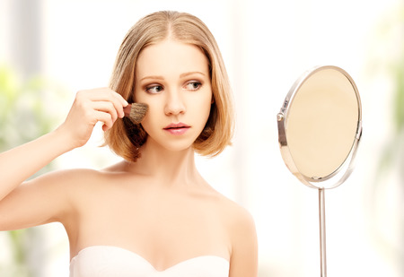 beautiful young woman doing  makeup with brush in the mirrorの写真素材