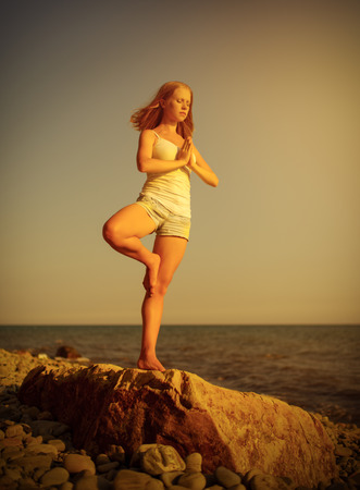 woman doing yoga on the beach by the sea at sunsetの写真素材