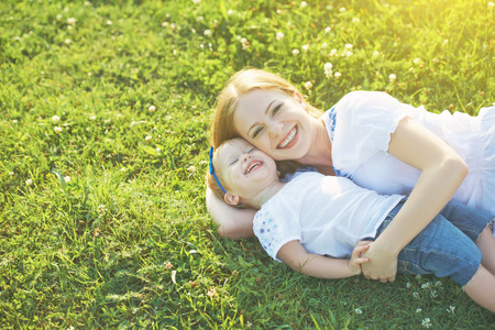 happy family on nature. mom and baby daughter lying are playing and laughing in the green grassの写真素材