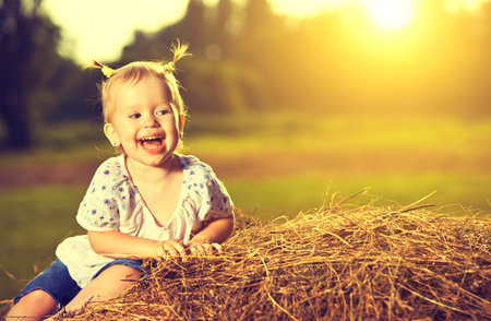 happy baby girl laughing on hay in summer at sunsetの写真素材