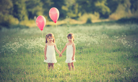 girls twin sisters in the meadow in the summer with balloonsの写真素材