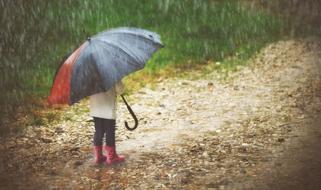 happy baby girl with an umbrella in the rain runs through the puddles